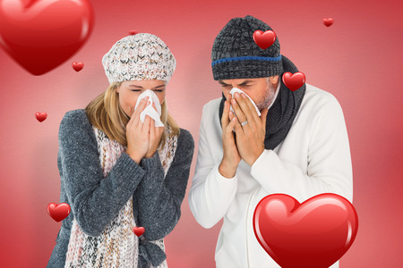 Sick couple in winter fashion sneezing against red vignetteの写真素材