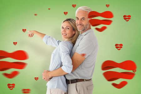 Happy couple smiling at camera and pointing against green vignetteの写真素材