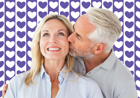 Affectionate man kissing his wife on the cheek  against valentines day patternの写真素材