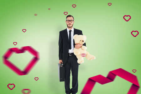 Geeky businessman holding briefcase and teddy against green vignetteの写真素材