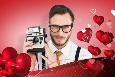 Geeky hipster holding a retro camera against red vignetteの写真素材