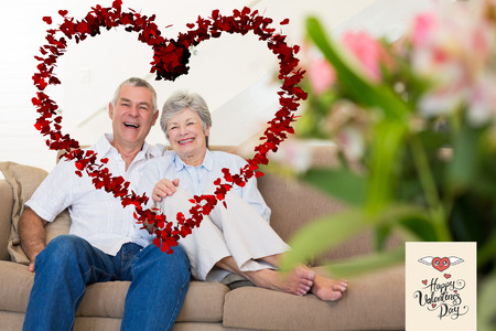 Happy senior couple relaxing on sofa against happy valentines dayの写真素材