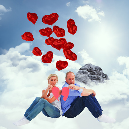 Sad mature couple holding a broken heart against mountain peak through the cloudsの写真素材