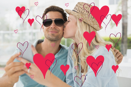 Hip young couple taking a selfie together against valentines day patternの写真素材