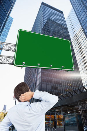 Thinking businessman scratching head against skyscraper in cityの写真素材