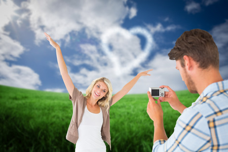 Man taking photo of his pretty girlfriend against green field under blue skyの写真素材