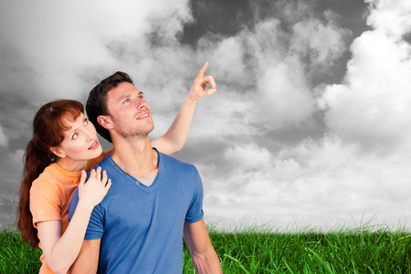 Happy couple looking upwards against green grass under grey skyの写真素材
