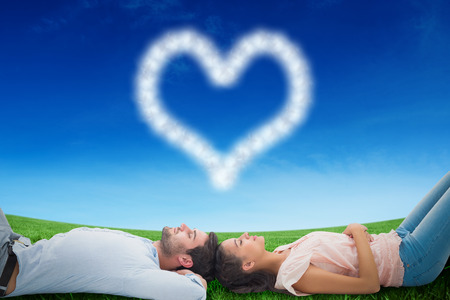 Attractive young couple lying down against green field under blue skyの写真素材