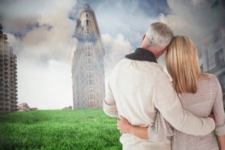 Happy couple standing with arms around against cloudy sky over cityの写真素材