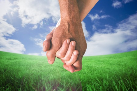 Happy senior couple holding hands against green field under blue skyの写真素材
