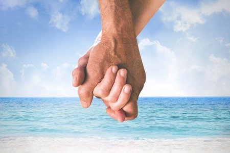 Happy senior couple holding hands against beach sceneの写真素材