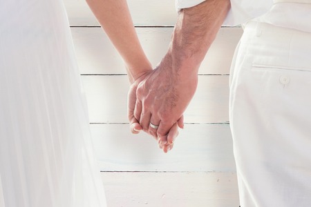 Bride and groom holding hands close up against painted blue wooden planksの写真素材
