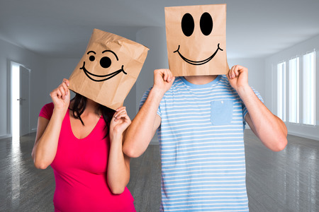 Young couple with bags over heads against bright room with wooden floorの写真素材
