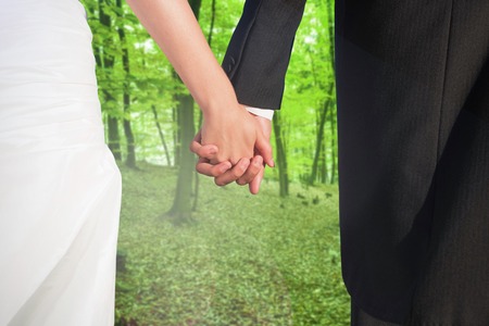 Close up of cute young newlyweds holding their hands against trees in the autumnal forestの写真素材
