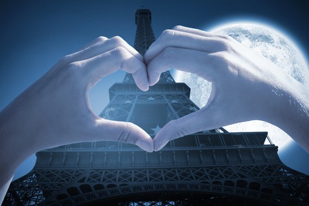 Hands making heart shape on the beach against large moon over eiffel towerの写真素材