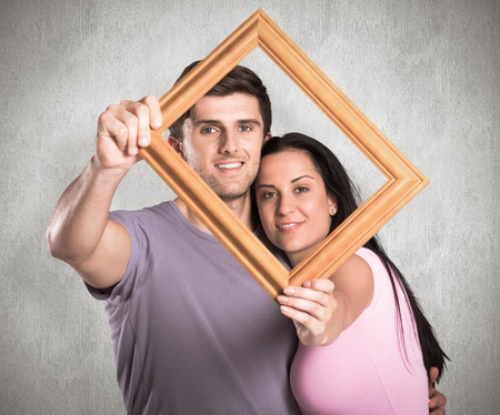 Young couple holding up frame against weathered surfaceの写真素材