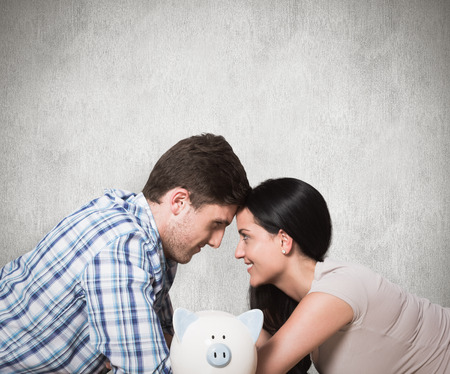 Young couple lying on floor smiling with piggy bank against weathered surfaceの写真素材