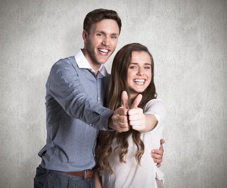 Happy couple gesturing thumbs up against weathered surfaceの写真素材