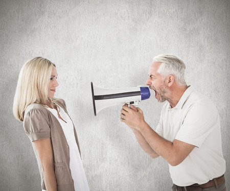 Angry man shouting at girlfriend through megaphone against weathered surfaceの写真素材