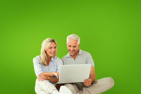 Happy couple sitting and using laptop against green vignetteの写真素材