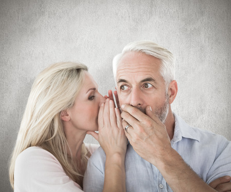 Woman whispering a secret to husband against weathered surfaceの写真素材