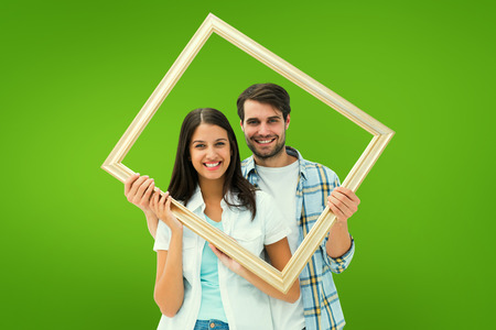 Happy young couple holding picture frame against green vignetteの写真素材