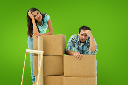 Stressed young couple with moving boxes against green vignette
