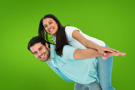 Happy casual man giving pretty girlfriend piggy back against green vignetteの写真素材