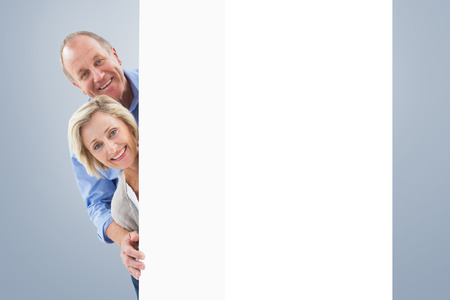Mature couple smiling behind wall against grey vignetteの写真素材