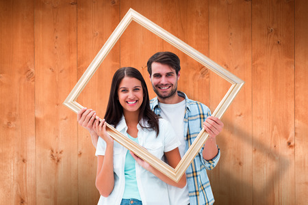 Happy young couple holding picture frame against wooden planksの写真素材