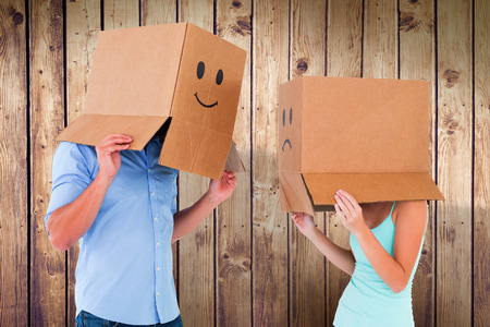 Couple wearing emoticon face boxes on their heads against wooden planksの写真素材