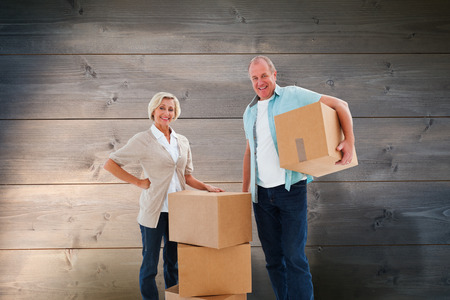 Older couple smiling at camera with moving boxes against bleached wooden planks backgroundの写真素材