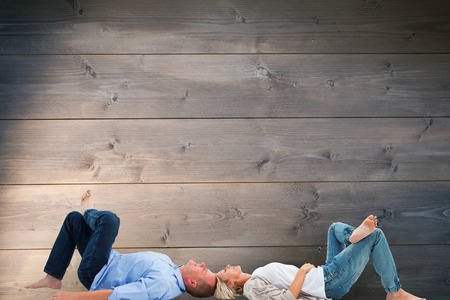 Mature couple lying and smiling against bleached wooden planks backgroundの写真素材