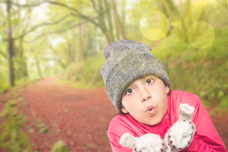 Wrapped up little girl blowing over hands against peaceful autumn scene in forestの写真素材
