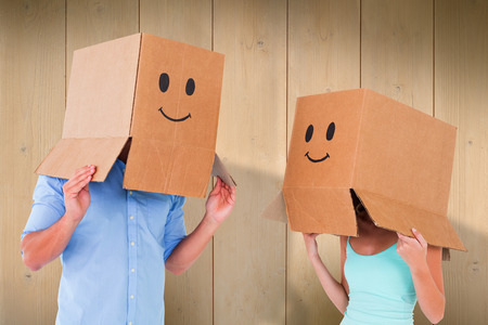 Couple wearing emoticon face boxes on their heads against wooden planksの写真素材