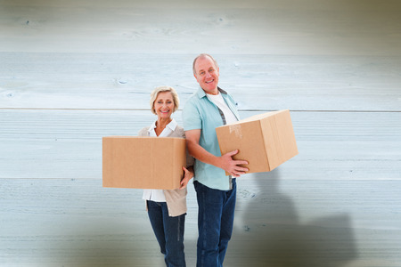 Older couple smiling at camera holding moving boxes against bleached wooden planks backgroundの写真素材