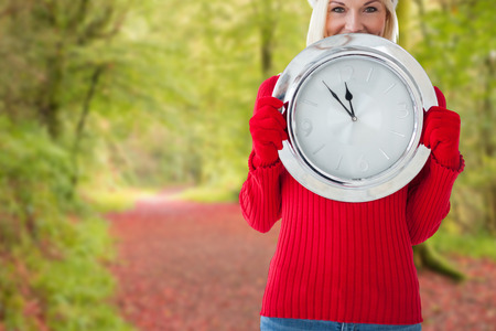 Happy festive blonde with clock against peaceful autumn scene in forest