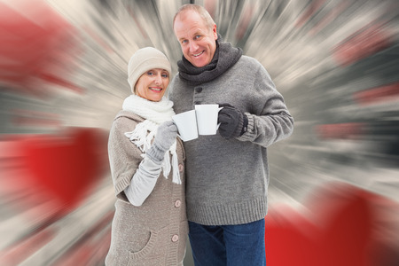 Happy mature couple in winter clothes holding mugs against love heart patternの写真素材