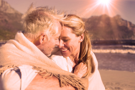 Smiling couple sitting on the beach under blanket on a sunny dayの写真素材