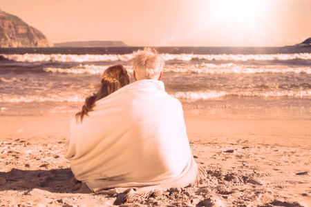 Couple sitting on the beach under blanket looking out to sea on a sunny dayの写真素材