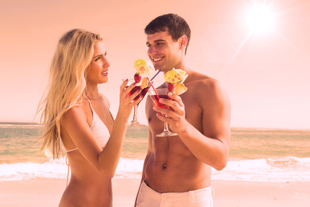 Happy young couple holding cocktails at the beachの写真素材