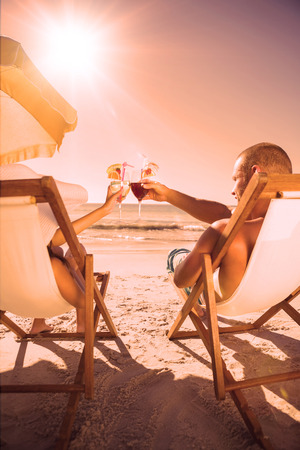 Couple on the beach clinking their glasses while relaxing on their deck chairsの写真素材