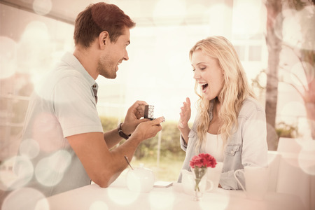 Man proposing marriage to his shocked blonde girlfriend on the cafe terrace on sunny day