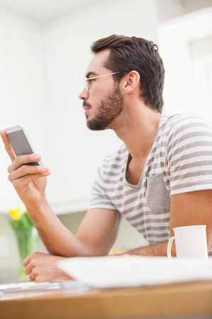 Young man using smartphone while having coffee at home in the kitchenの写真素材