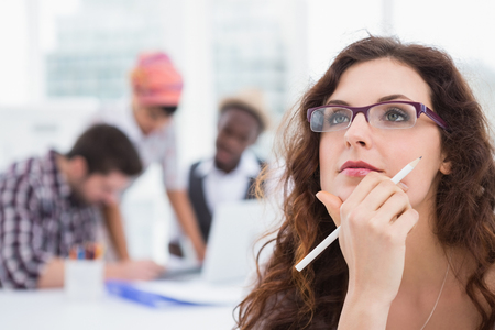 Portrait of businesswoman with glasses thinking with colleagues behind herの写真素材
