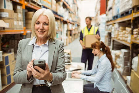 Smiling warehouse manager using handheld in a large warehouse