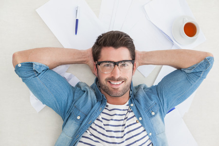 Relaxed businessman lying on paper on the floor in the officeの写真素材