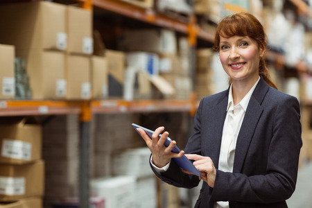 Smiling businesswoman scrolling on digital tablet in a large warehouseの写真素材