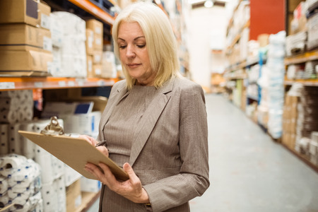 Focused female manager holding clipboard in a large warehouseの写真素材