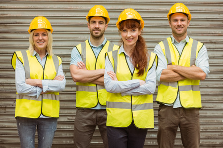 Warehouse team with arms crossed wearing hard hat in a large warehouseの写真素材